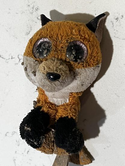 A small, dirty stuffed fox with large plastic eyes