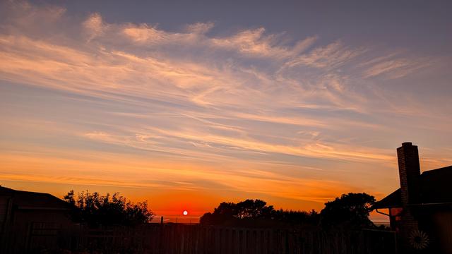 An orange sky with wispy clouds at sunset.