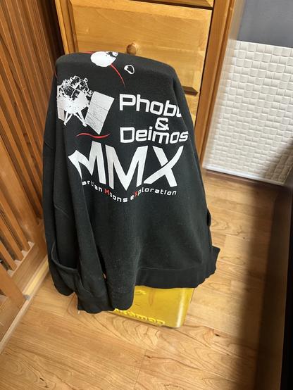 A sweater with the logo for the Martian Moons eXploration (MMX) on the back is draped over a suitcase.