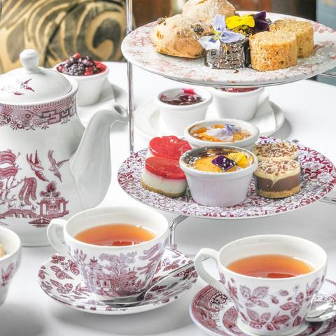 a china teapot, two cups of tea, and a rack of pastries, all in a matching pattern.