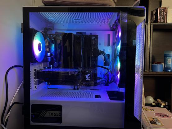 a PC case, viewed from the side. you can see inside from its glass door. there’s some rainbow lights coming from the case fans.