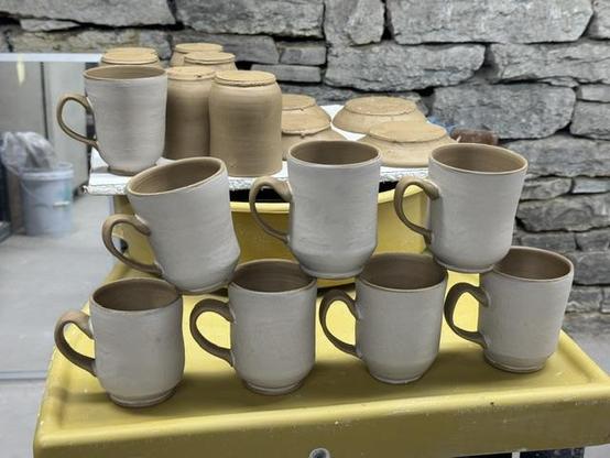 A stack of hand thrown cups. More cups and saucers are in the background