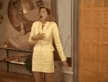 a woman in a yellow suit is standing in front of a door . She faints and falls to the floor.