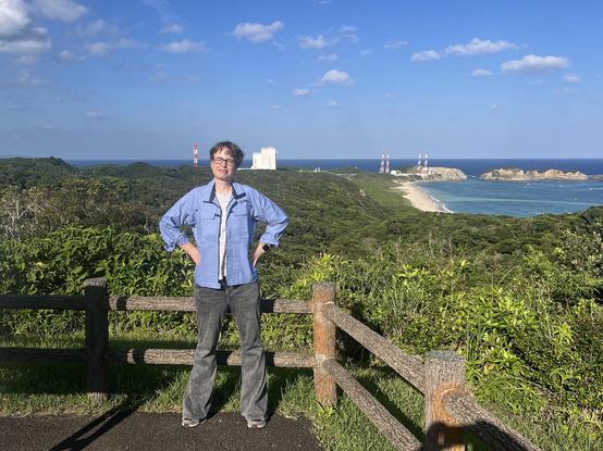 A photograph of me standing on a lookout spot at JAXA’s Tanegashima Space Center. Behind me, by the sea, is the launch pad.