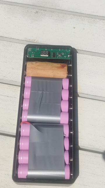 A housing with eight recovered 18650 lithium cells, a small USB charge controller, and a shim of wood where two more cells would usually go.