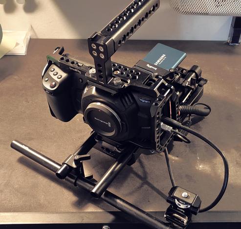 I video camera rig with a metal cage around the camera, a  carrying handle, multiple rails for accessories, and a big battery pack and an SSD mounted in the back