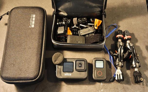 GoPro Hero 9 action camera in a cage with a big mic on it, a remote control, two articulated mounting arms, and a bag full of little mounting accessories