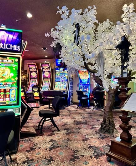 Inside a casino. slot machines on the left, an artificial tree with white leaves. colorful floral carpet.