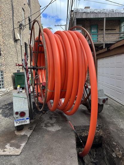 A huge orange tube on a reel plugged into a hole in the pavement