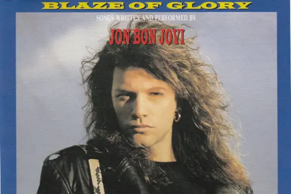 the cover of the number 1 single 'Blaze of Glory' by Jon Bon Jovi the image features a blue border, and Bon Jovi from the chest up looking directly at the viewer, wearing a black leather jacket and sporting giant 80s hair metal hair and backdropped by a cloudy sky.