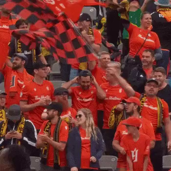 A gif of soccer fans, mainly dressed in orange. Cheering for Forge FC.  Lots of waving flags including a pride flag.