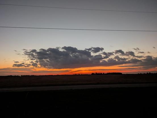 Sunrise over the corn field. Not today. A layer of dark orange light is capped by one large, broken cloud. Above, pale blue fades to gray.