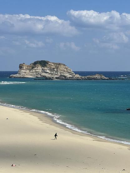 A lone figure in a black jacket walking along the beach towards the sea.
