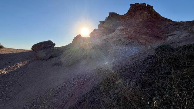 A rocky mountain with a blue sky and the sun shining brightly.