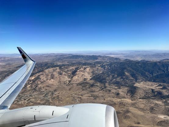 Looking out an airplane window shortly after takeoff. Mountains and clear blue skies.