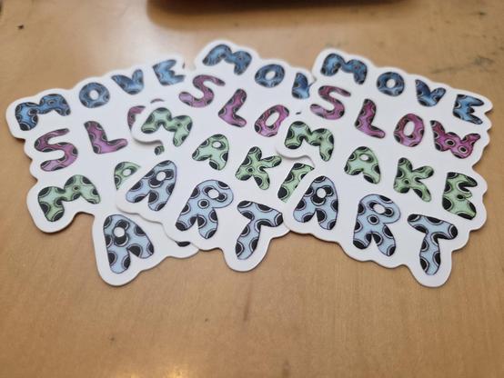 a small scattering of stickers made from my hand drawn art with puffy text that reads "Move slow make art"