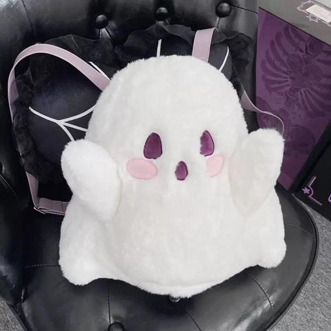 A cute, fluffy white ghost plush backpack sitting on a black leather chair. The ghost has purple embroidered eyes, a small purple mouth, pink rosy cheeks, and light purple backpack straps.