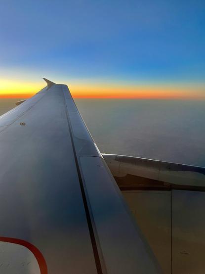 Looking out an airplane window at the left wing and engine as the sun sets off to the left and behind the airplane.