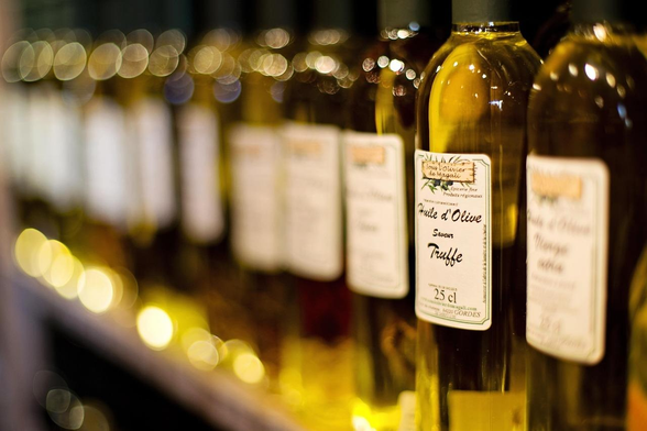 A likely AI generated imaged of a shelf of olive oil. One bottle is in "focus", but the label is at a weird angle to the bottle. The label purports to be from "Sous l'Olivier  de Magali", and reads "Huile d'Olive Saveur Truffe" (25cl).