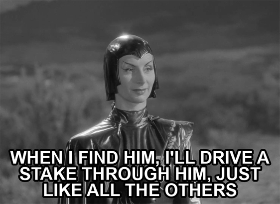 screenshot from the film Devil Girl From Mars showing a serious woman wearing a black leather suit, cape, and cowl. Text reads: "When I find him, I'll drive a stake through him, just like all the others"