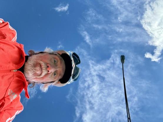 The last mile of the trip coming into downtown Albany, phone camera looking straight up into blue sky, wispy clouds, light pole, and me. I'm wearing a bright orange windbreaker, helmet with visor and sunglasses jammed into vents, have white beard and a semi-wild look. Mostly I'm just thinking about eating and crashing onto a soft bed.