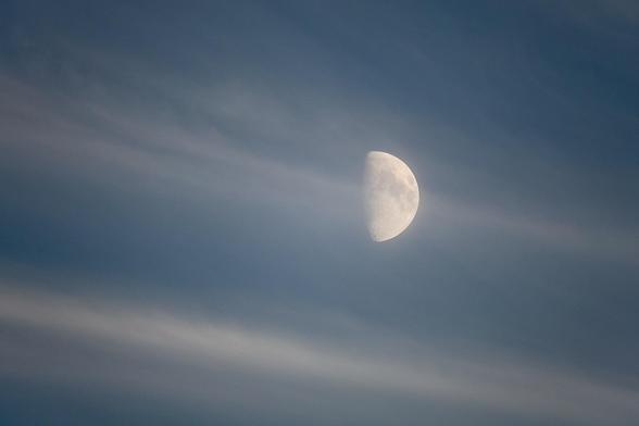 A half-visible moon is set against a blue sky with soft, wispy clouds.