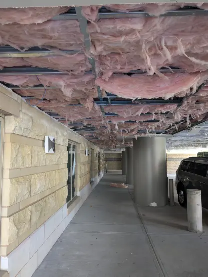 Photo of a covered parking area where the ceiling has been torn open revealing pink fiberglass insulation