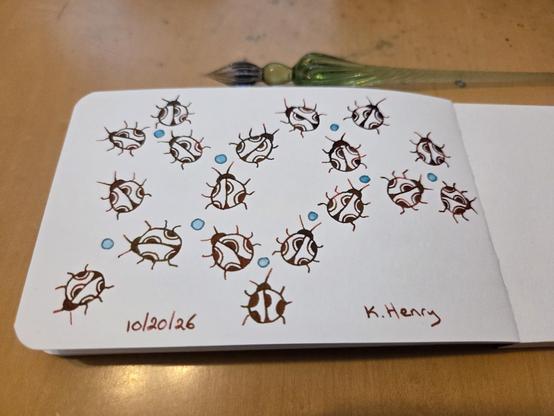 Hand drawn generative/procedural art in ink on an open page of my sketchbook. The abstract pattern looks a bit like ladybugs with polka dots arranged in a branching pattern. My glass dipping pen is next to my sketchbook.