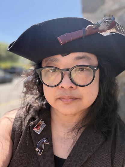 A woman with glasses and a pirate hat. Blue sky behind. It is bright!!!
