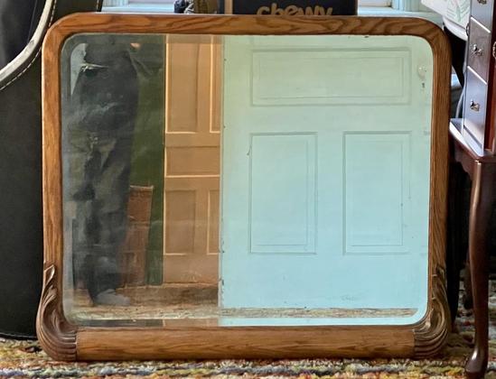 A big antique mirror of the sort you put above a dresser, in an oak wood frame with graceful carved decorations at the lower corners