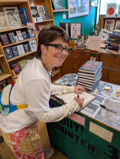 I am smiling and signing books at the counter in Green Apple Books on Clement Street