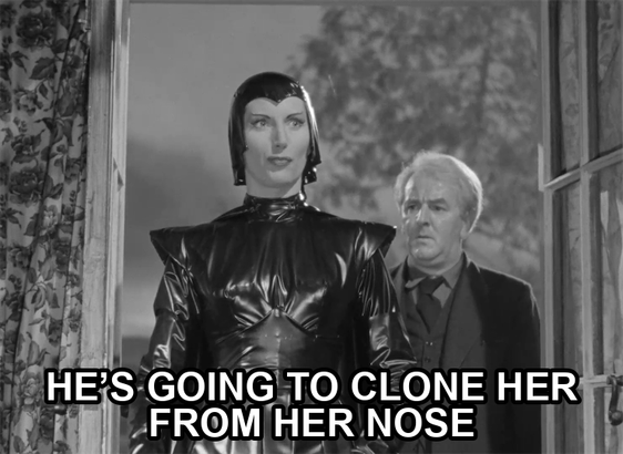 screenshot from the film Devil Girl From Mars showing a serious woman wearing a black leather suit, cape, and cowl. Text reads: "He’s going to clone her from her nose"