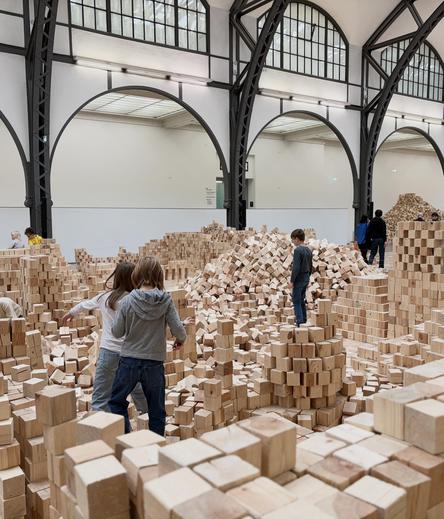 A group of kids standing in a see of wooden blocks and build walls and other things