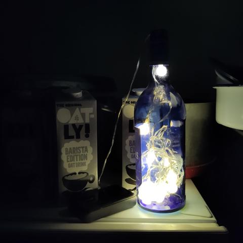 A sherry bottle full of string lights connected to a power bank