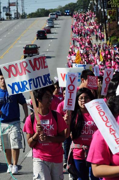 protesters walking down the side of the road holding signs like "vote" "educate" and "your vote your future"