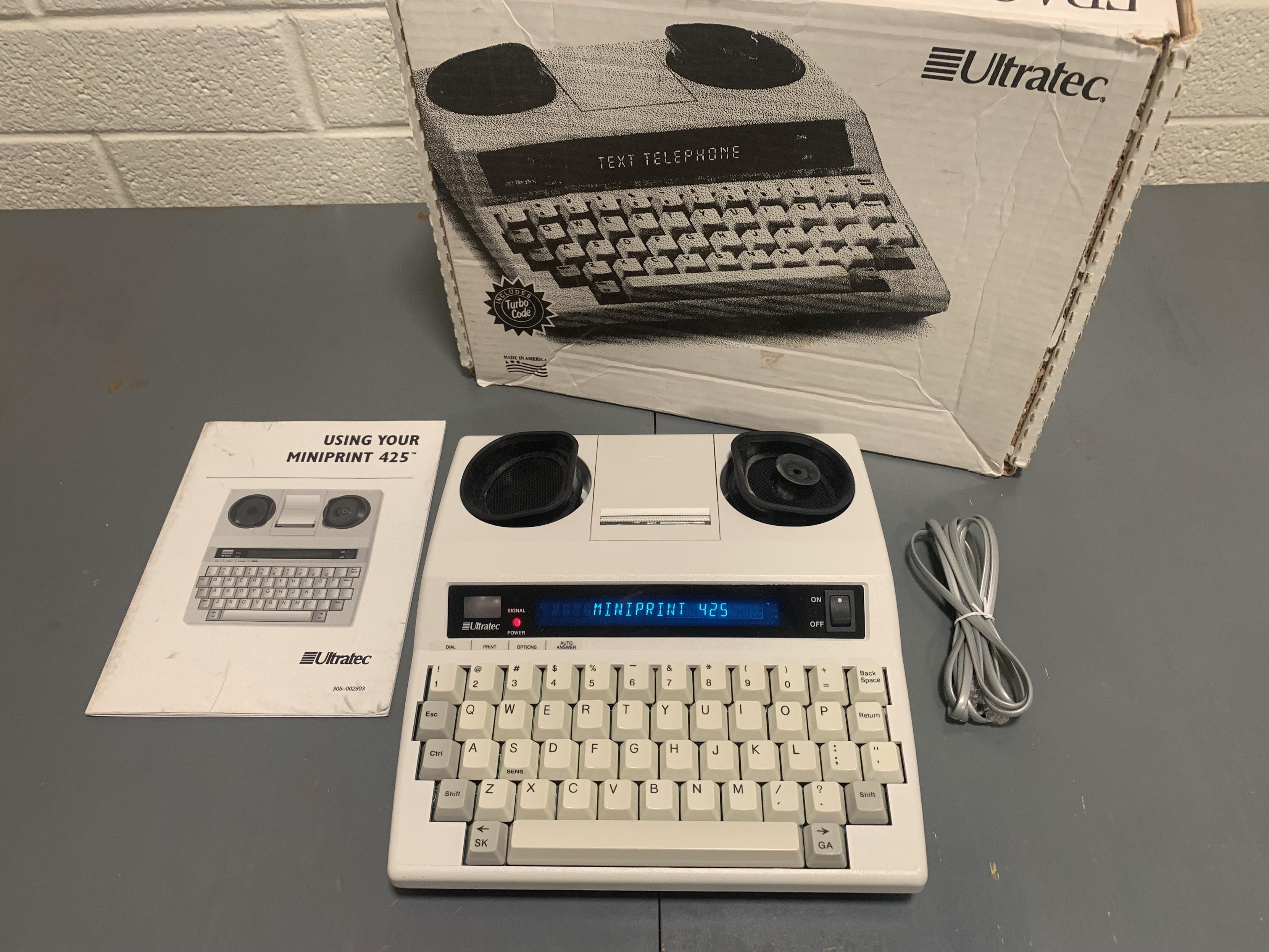 An Ultratec Miniprint 425 with MINIPRINT 425 displayed digitally and no paper loaded, its manual, phone cable, and box.